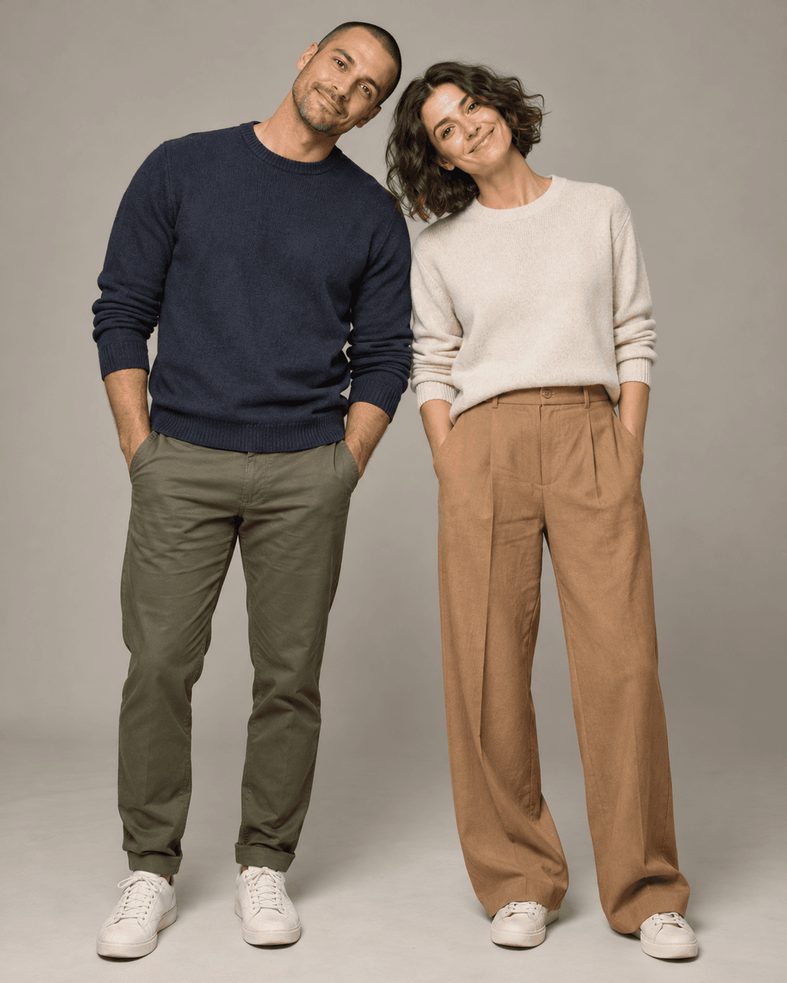 AI-generated concept of two fictional adults standing on level ground against a neutral studio background, each tilting their head inward toward the other, relaxed knitwear and trousers.