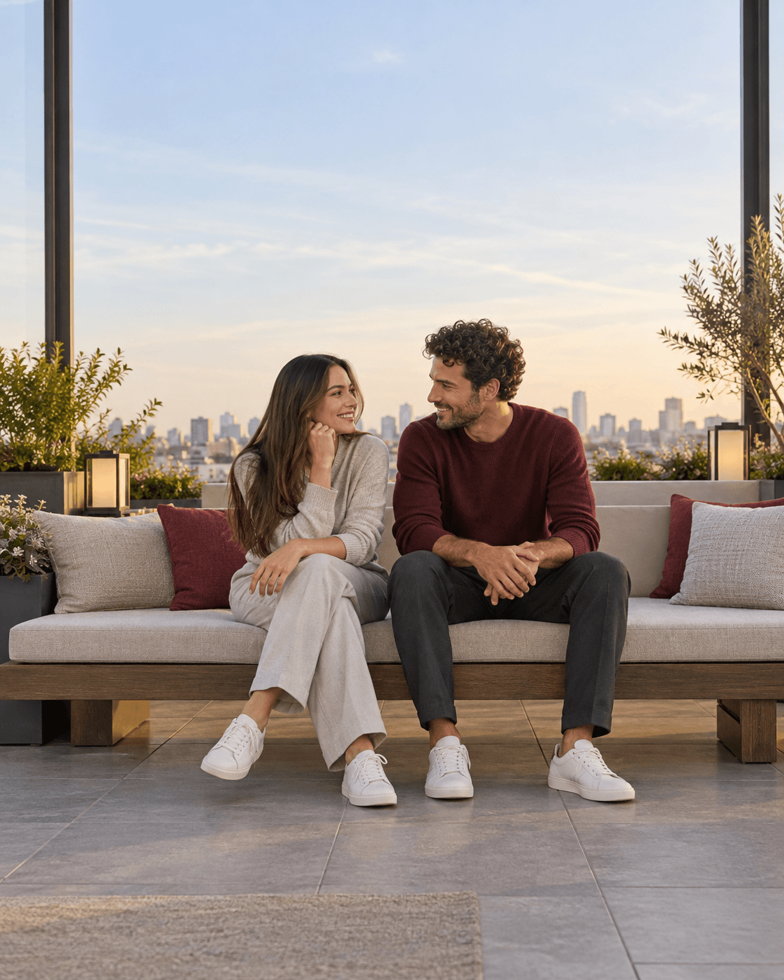 AI-generated concept: two fictional adults seated side by side on a broad bench well inside an enclosed rooftop terrace, low generic skyline and wide pale sky, light gray and burgundy outfits, clear feet and seat support.