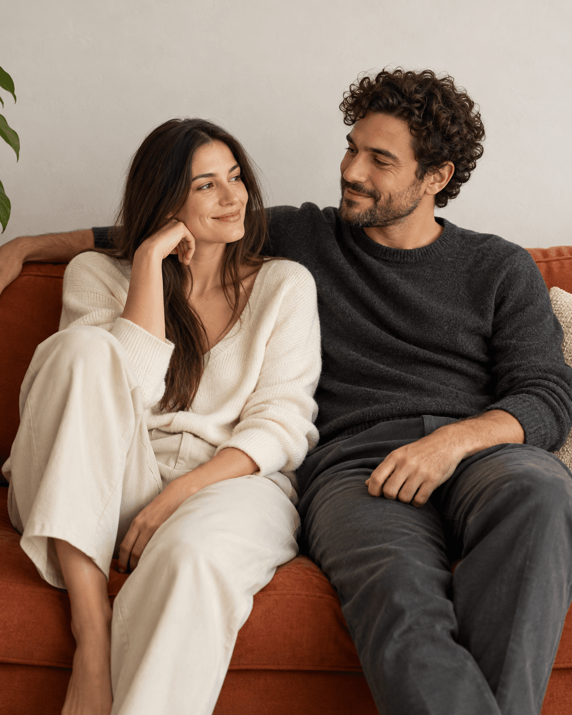 AI-generated concept: two fictional adults seated comfortably on a terracotta sofa against a pale wall, casual cream and charcoal clothes, three-quarter crop, no logos or personal documents.