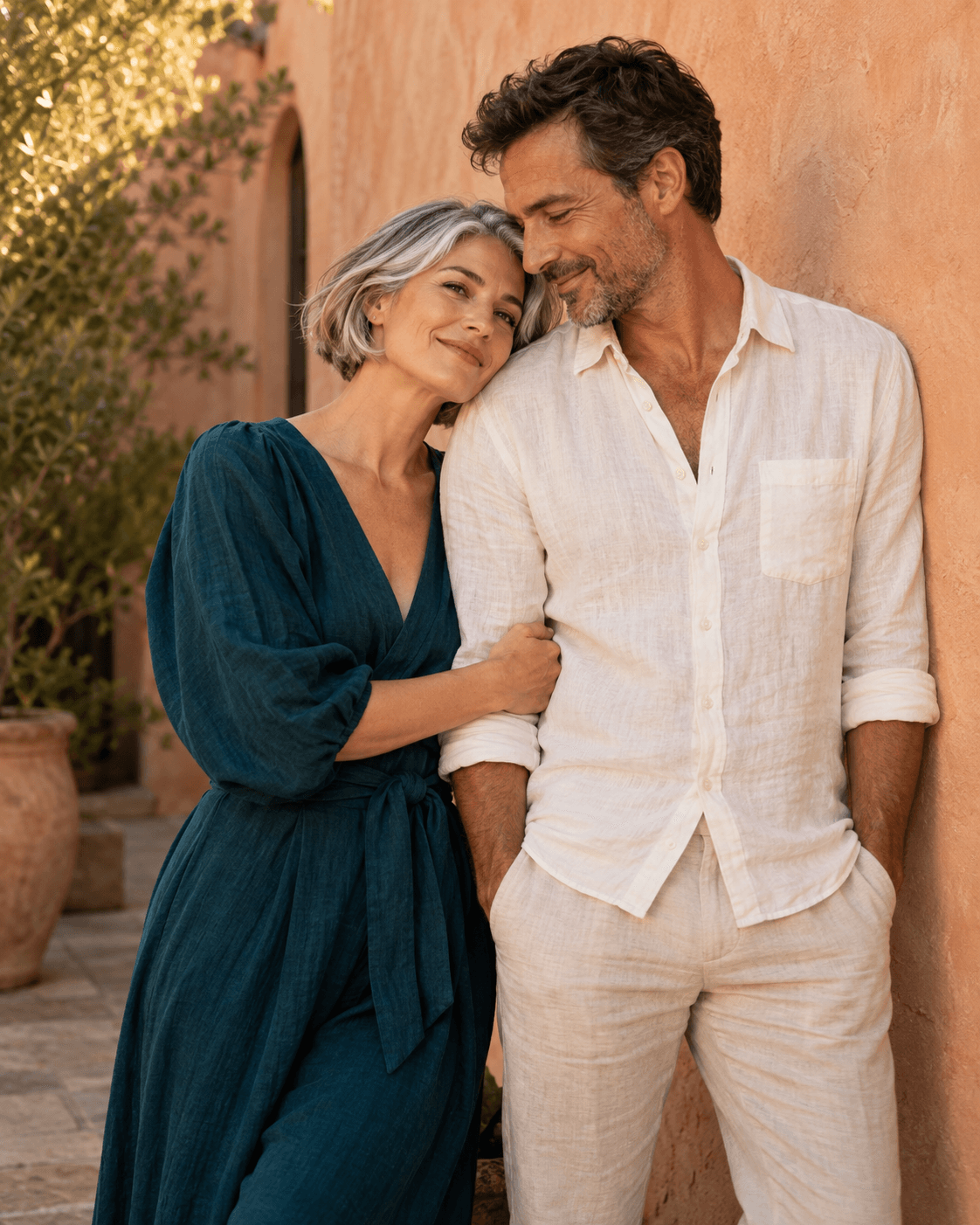 AI-generated concept: two fictional adults beside a pale terracotta courtyard wall, warm evening light, one deep teal outfit and one cream outfit, unbranded generic setting.