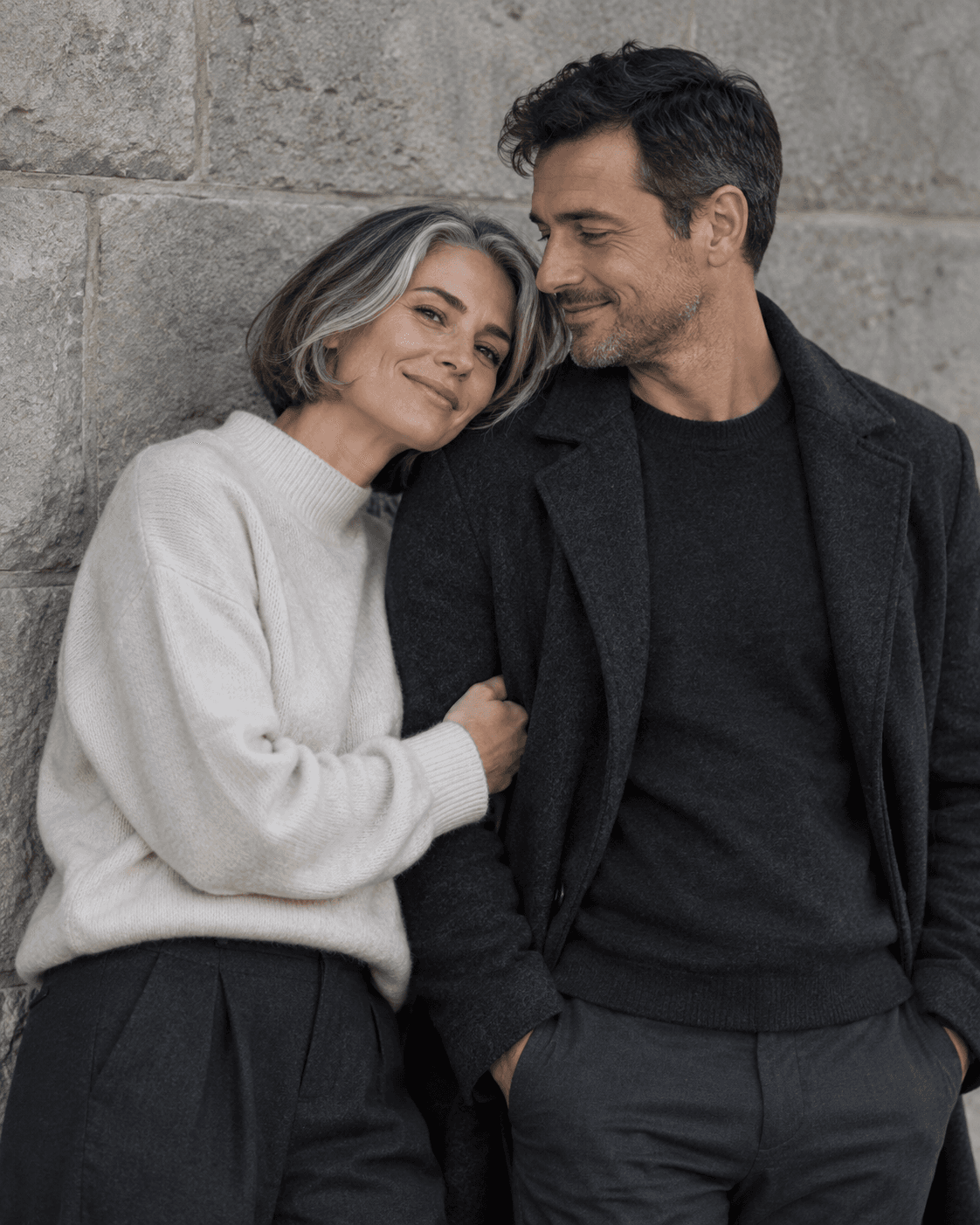 AI-generated concept: two fictional adults beside a plain stone wall in open shade, subtle cool muted tones, medium portrait, fine grain, charcoal and soft cream clothes.