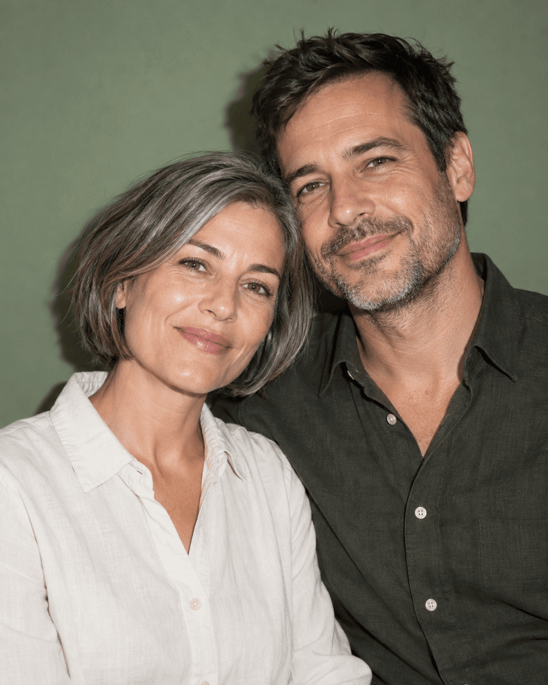 AI-generated concept: two fictional adults chest-up against a muted green plain wall, direct-flash-inspired frontal light, one coherent subtle shadow, plain shirts, relaxed expressions, controlled skin highlights.