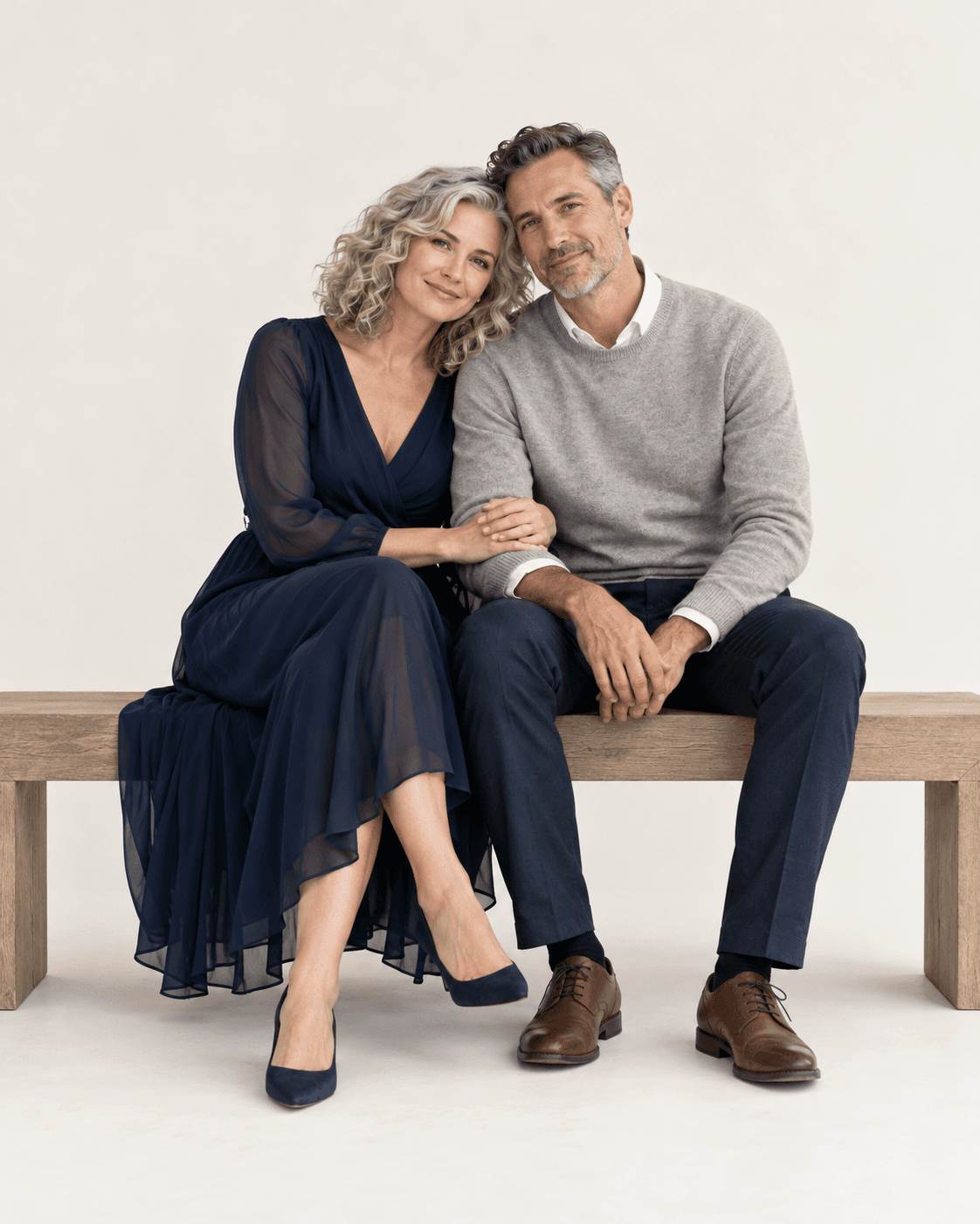 AI-generated concept: two fictional adults seated on a broad plain bench against an off-white seamless backdrop, small inward lean, dark blue and soft gray outfits, clear contact points, ample empty space.