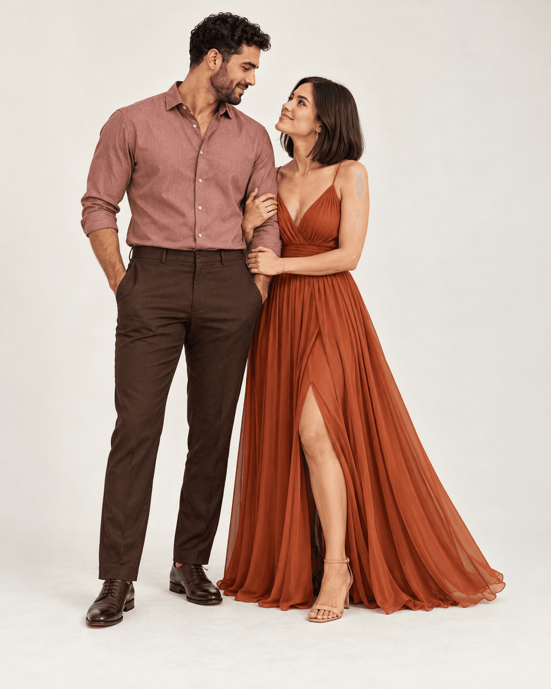 AI-generated full-length studio concept of two fictional adults: Person A wears a flowing rust dress; Person B wears a muted rose shirt and deep brown trousers.