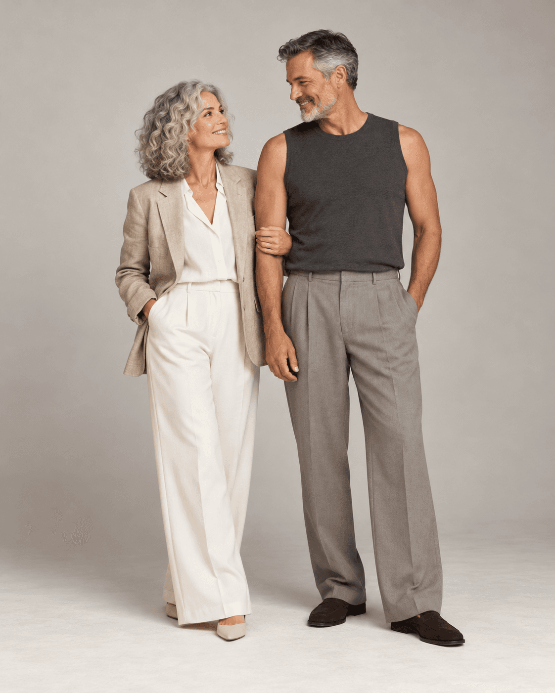 AI-generated full-length studio concept of two fictional adults: Person A wears sand-and-cream light tailoring; Person B wears a charcoal sleeveless top and warm-gray fluid trousers.